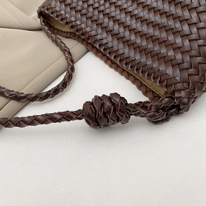 Detail of dark brown woven leather bucket bag with handcrafted knot on the shoulder strap