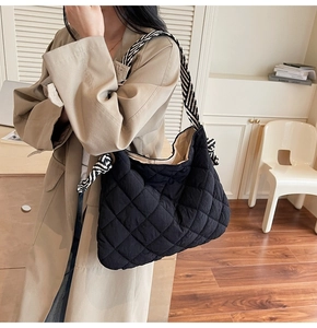 Detail of black quilted tote bag with striped straps shown on a beige trench coat