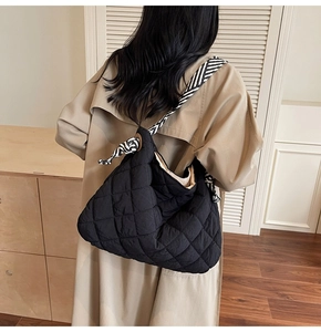 Detail of black quilted puffer tote bag with striped woven strap on fashion model