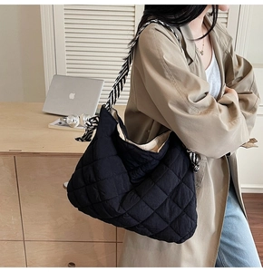 Detail of black quilted hobo bag with textured stitching and striped woven shoulder strap