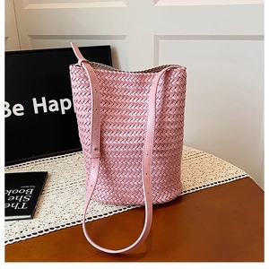 Detail of pink hand-woven bucket bag with diamond lattice pattern on a wooden table