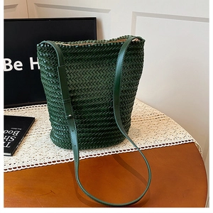 Detailed view of dark green woven bucket bag with fine strap on wooden desk