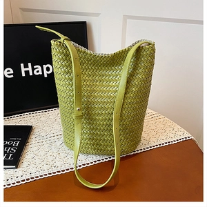 Detail of lime green hand-woven bucket bag with adjustable shoulder strap on a table