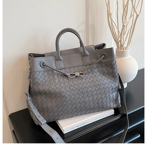 Close-up of woven grey leather tote bag texture with elegant metallic bow clasp detail