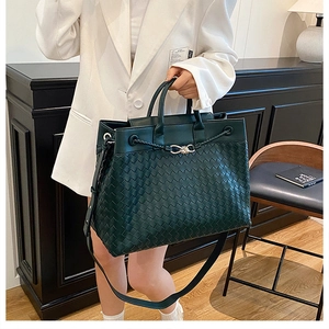 Detail of hand-woven dark green tote bag with metal knot clasp and leather texture