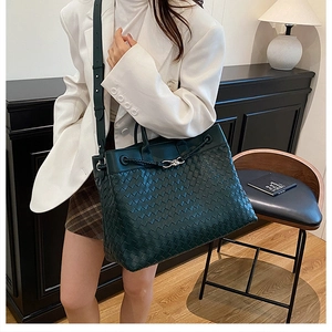 Detail of dark green hand-woven leather tote bag featuring a silver metal twist lock buckle