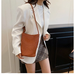 Detailed texture of brown hand-woven bucket bag with slim shoulder strap on model