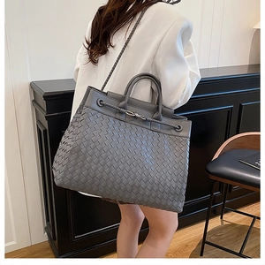 Detail of grey woven tote bag with metallic knot clasp shown in a professional setting