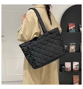 Quilted black tote bag with diamond pattern shown on model in a minimalist setting