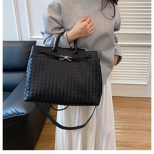 Detail of hand-woven black leather tote bag with metallic knot clasp and shoulder strap