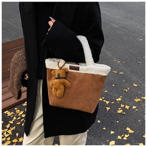 Detail of a brown suede handbag with white faux fur trim and a plush bear charm outdoors
