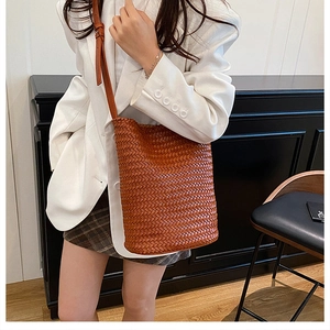 Detail of hand-woven brown bucket bag with adjustable leather strap on model