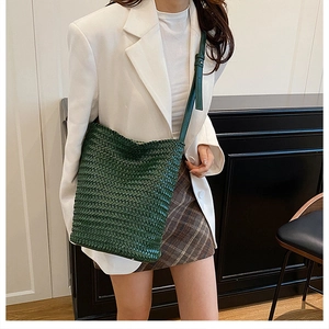 Detail shot of a dark green woven bucket bag in premium leather texture worn over the shoulder