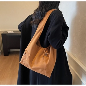 Detail of tan suede hobo bag featuring side drawstring knot and metal ring accents