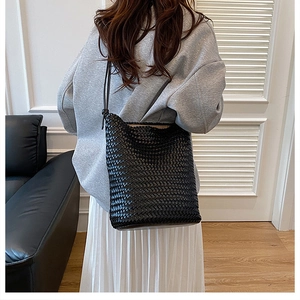 Detail of hand-woven black leather tote bag with fine geometric texture and slim shoulder strap