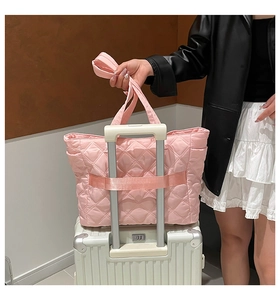 Pink quilted tote bag with luggage strap fixed on a suitcase handle for travel use