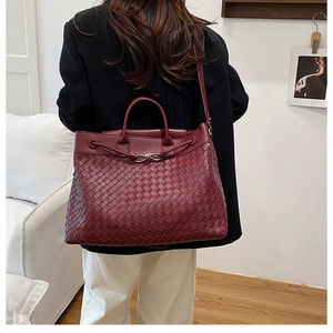 Detail of burgundy hand-woven leather tote bag with knotted buckle and woven texture