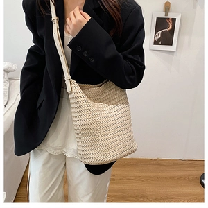 Detail of beige hand-woven hobo bucket bag with leather strap on a model in a black suit