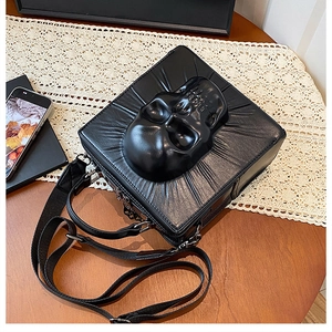 Macro view of gothic black square crossbody bag with 3D skull relief and wide strap