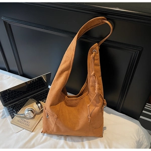 Brown faux suede hobo bag with drawstring details and metal hardware on white bedding