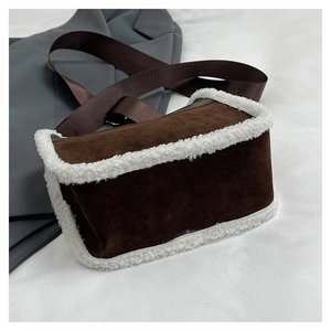 Detailed shot of brown suede crossbody bag with white faux fur trim on white fabric