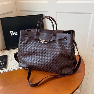 Handwoven dark brown tote bag with metal bow detail on a wooden table with lace mat
