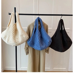 Detailed knit tote bags in beige, royal blue, and dark brown hanging on a rack