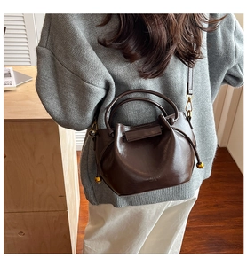 Detail of dark brown glossy PU leather bucket bag with gold ball drawstring and logo