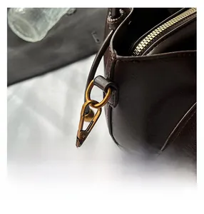 Detail of dark brown leather bucket bag showing metal zipper and vintage gold buckle
