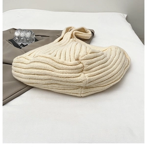 Detail view of cream white knit tote bag with ribbed texture on soft bedding