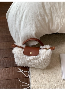 Close-up of white faux shearling handbag with brown leather handles on soft bedding