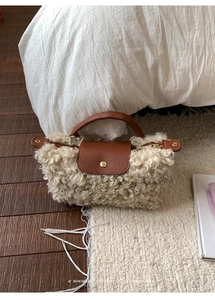 Detail of beige faux shearling handbag with brown leather flap and textured metal snap