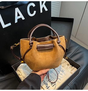 Close-up of brown suede drawstring bucket bag with leather handle and gold hardware detail