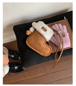 Detail of boot-shaped suede crossbody bag with white faux fur trim on a black bench