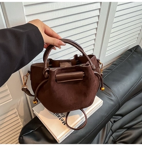 Macro shot of dark brown suede bucket bag with drawstring closure and gold metal ball detail