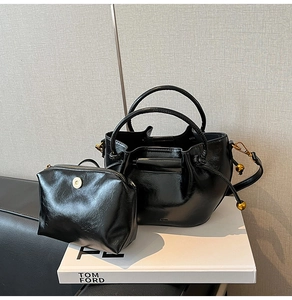Detail of black glossy bucket bag and small zipper pouch set with gold hardware