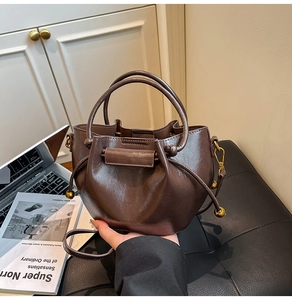Detail of brown leather bucket bag with gold spherical drawstring accents and dual handles