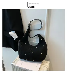 Detail view of black faux suede tote bag featuring metallic rivets on a suitcase