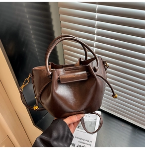 Detail of coffee brown leather bucket bag with debossed logo and gold metal hooks