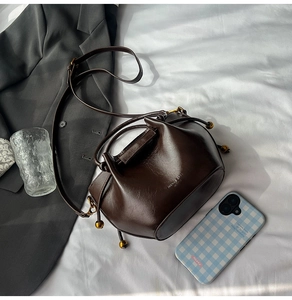 Macro detail of dark brown bucket bag with shiny PU leather finish and gold drawstring beads