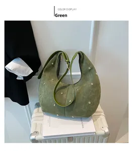 Detail of green suede hobo bag with gold rivet studs on white luggage surface