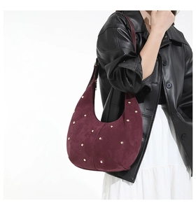 Detail of burgundy suede hobo bag with gold studs on a model in black leather jacket