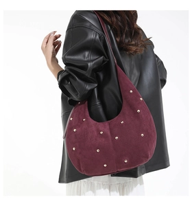 Detail of burgundy suede hobo bag with gold studs worn on shoulder for style and scale