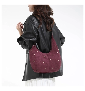 Detail view of burgundy suede crescent bag with gold rivets worn by a model