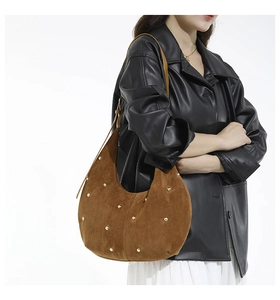 Detail of brown suede crescent bag with gold rivet studs and leather shoulder strap