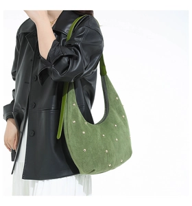 Chic green suede hobo bag with round gold rivets worn over a stylish black leather jacket