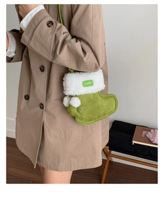 Detail shot of a green plush sock-shaped crossbody bag with white fur trim on a model