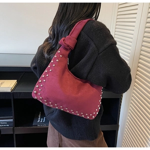 Close-up of wine red suede underarm bag featuring silver rivets and knotted handle detail