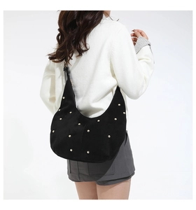 Close-up of black suede moon bag featuring gold rivet studs and slender leather shoulder strap