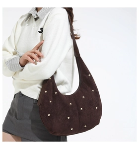 Close-up of brown suede hobo bag with gold metal studs on a model with white background